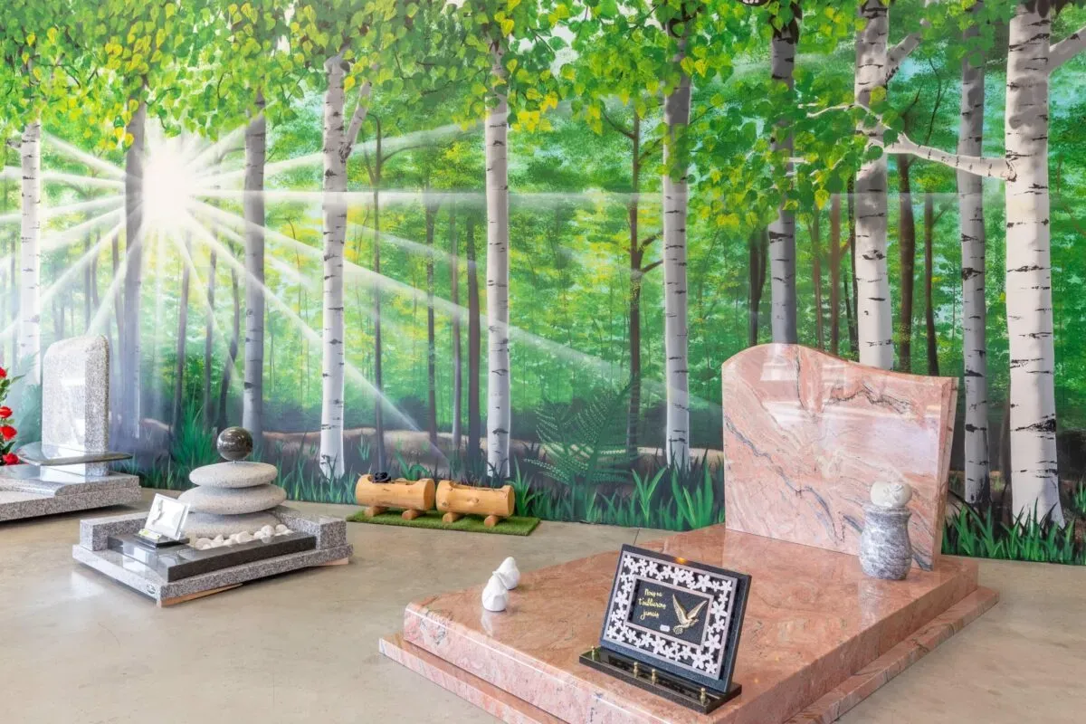 Monuments funéraires en granit rose et gris devant une fresque de forêt.